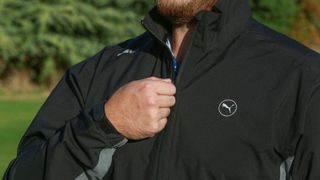 A man zips up the Puma DRYLBL Waterproof Golf Rain Jacket
