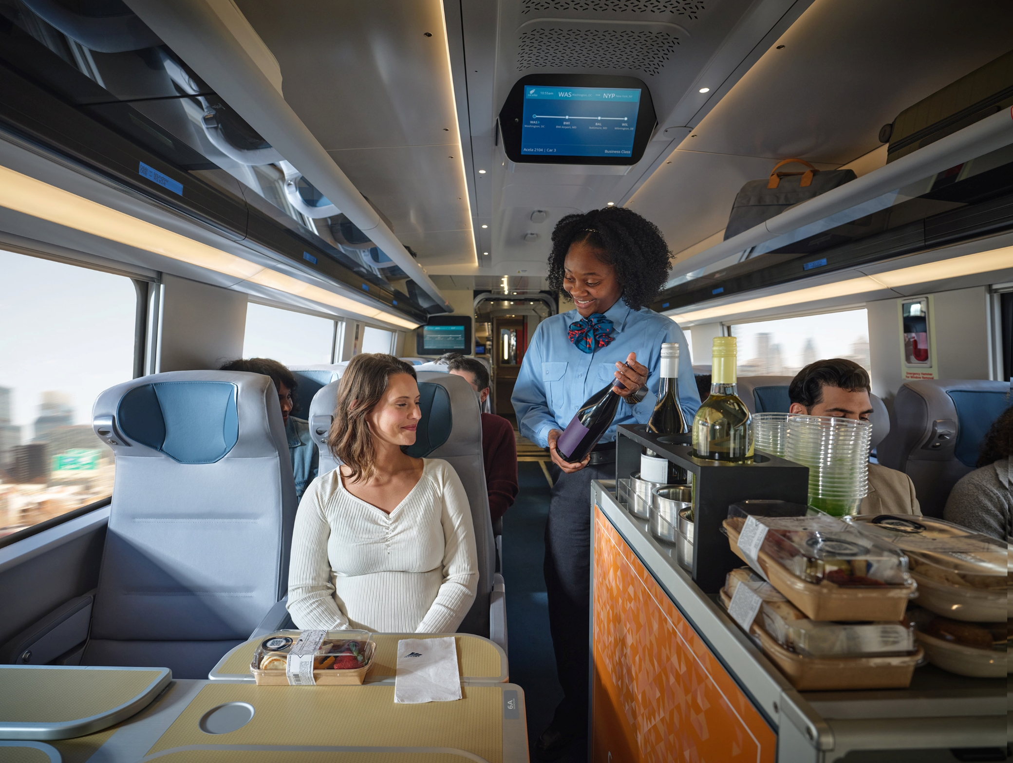 An attendant serving wine to a passenger on an Amtrak Acela train.