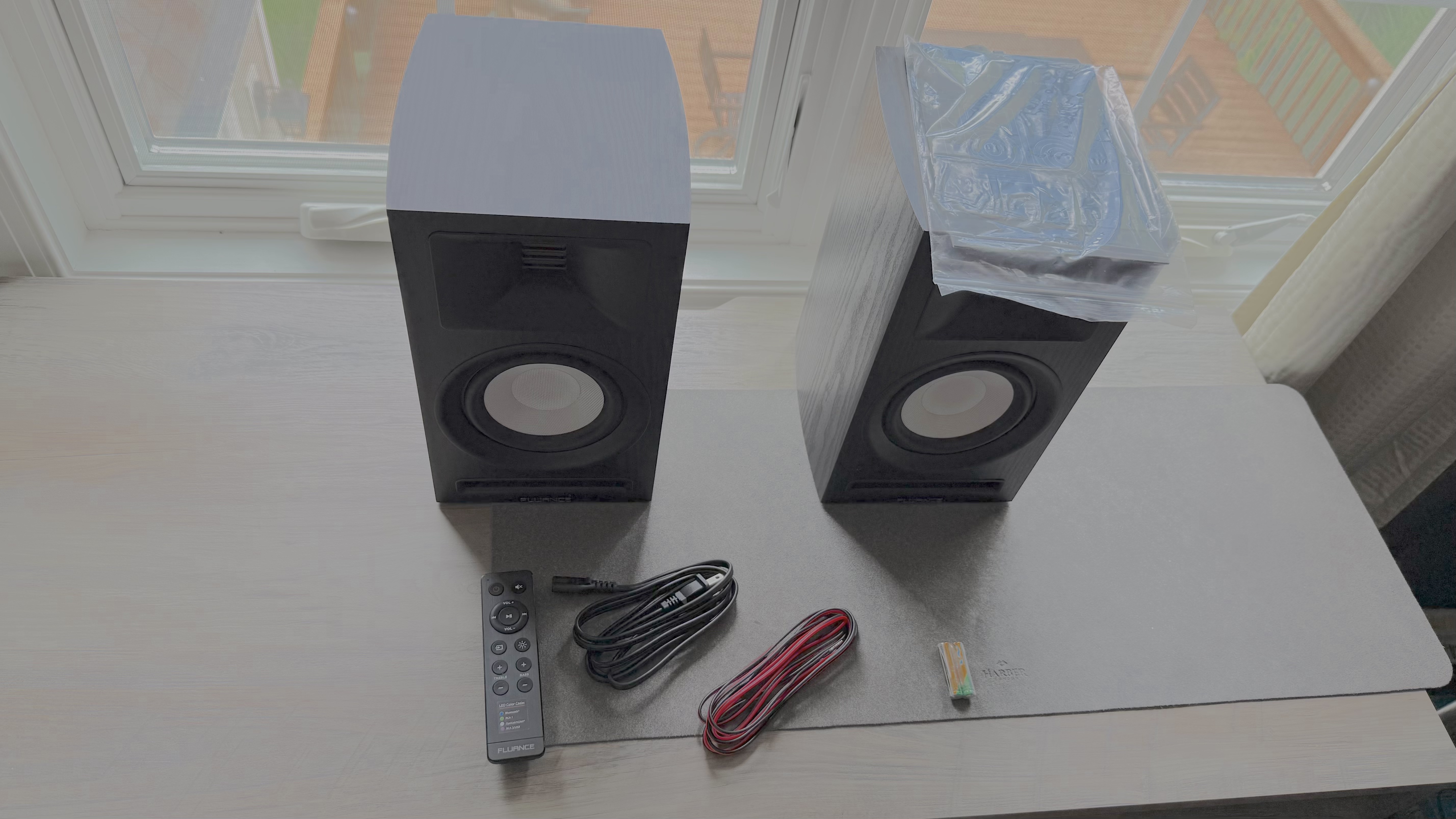 Black Fluance Ri71 bookshelf speakers on a windowsill, with supplied cables and remote control.