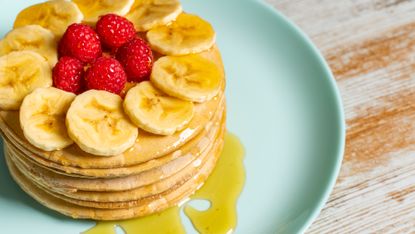 A stack of pancakes topped with syrup, banana slices and raspberries