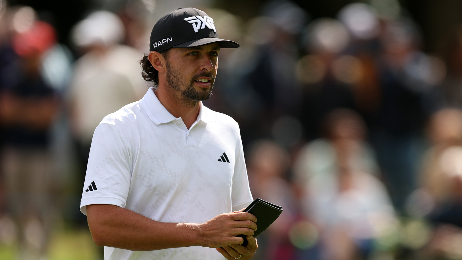 Marco Penge walks down the fairway holding a yardage book