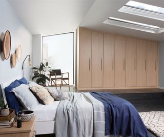 pale wooden fitted wardrobes in bedroom with sloped ceiling, rooflights and large picture window on one wall