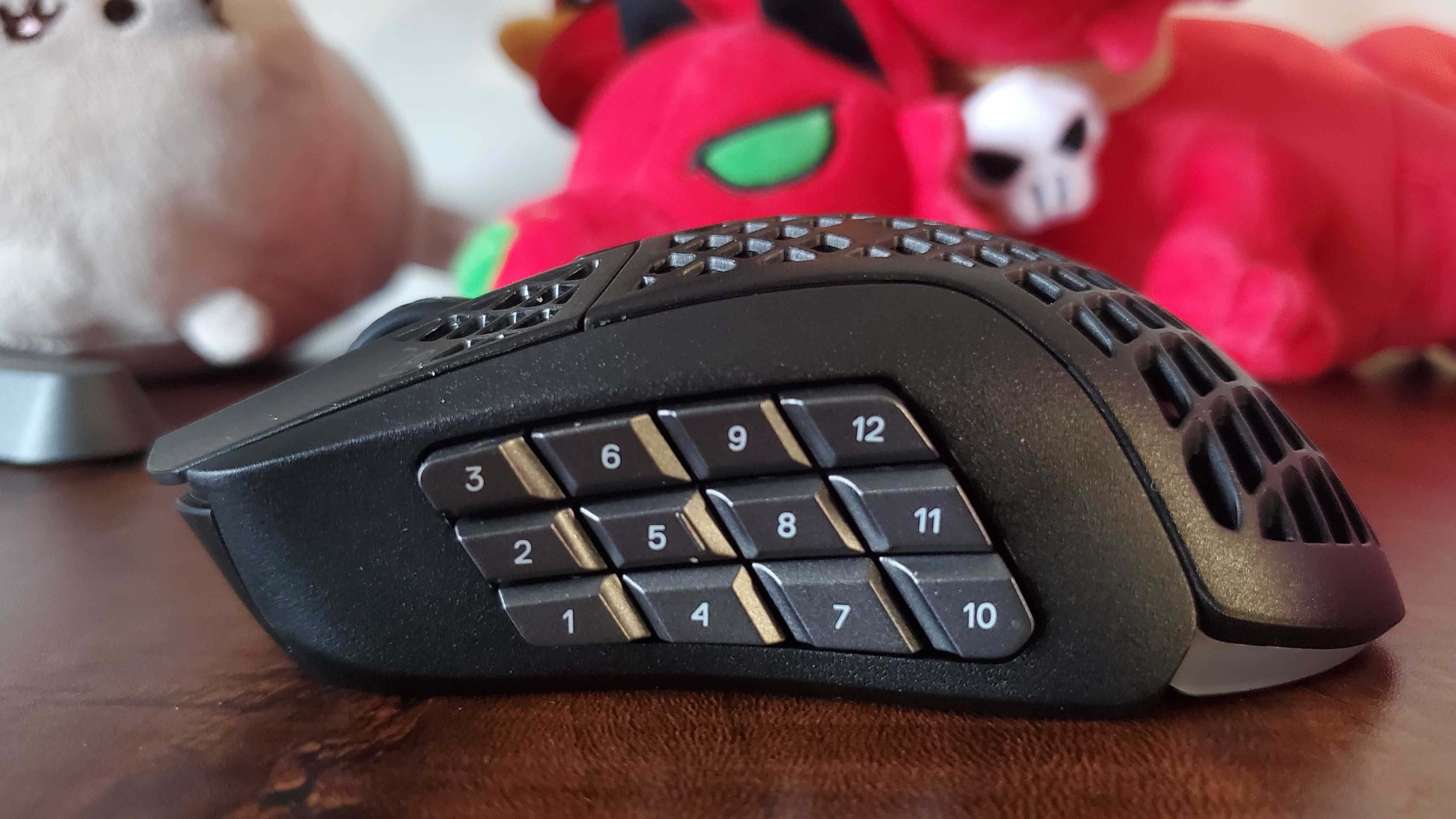 SteelSeries Aerox 9 on a dark wood desk next to some plushies