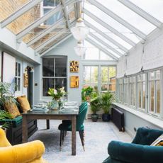 A conservatory with a dining and living areas and neutral-coloured Roman blinds covering the windows