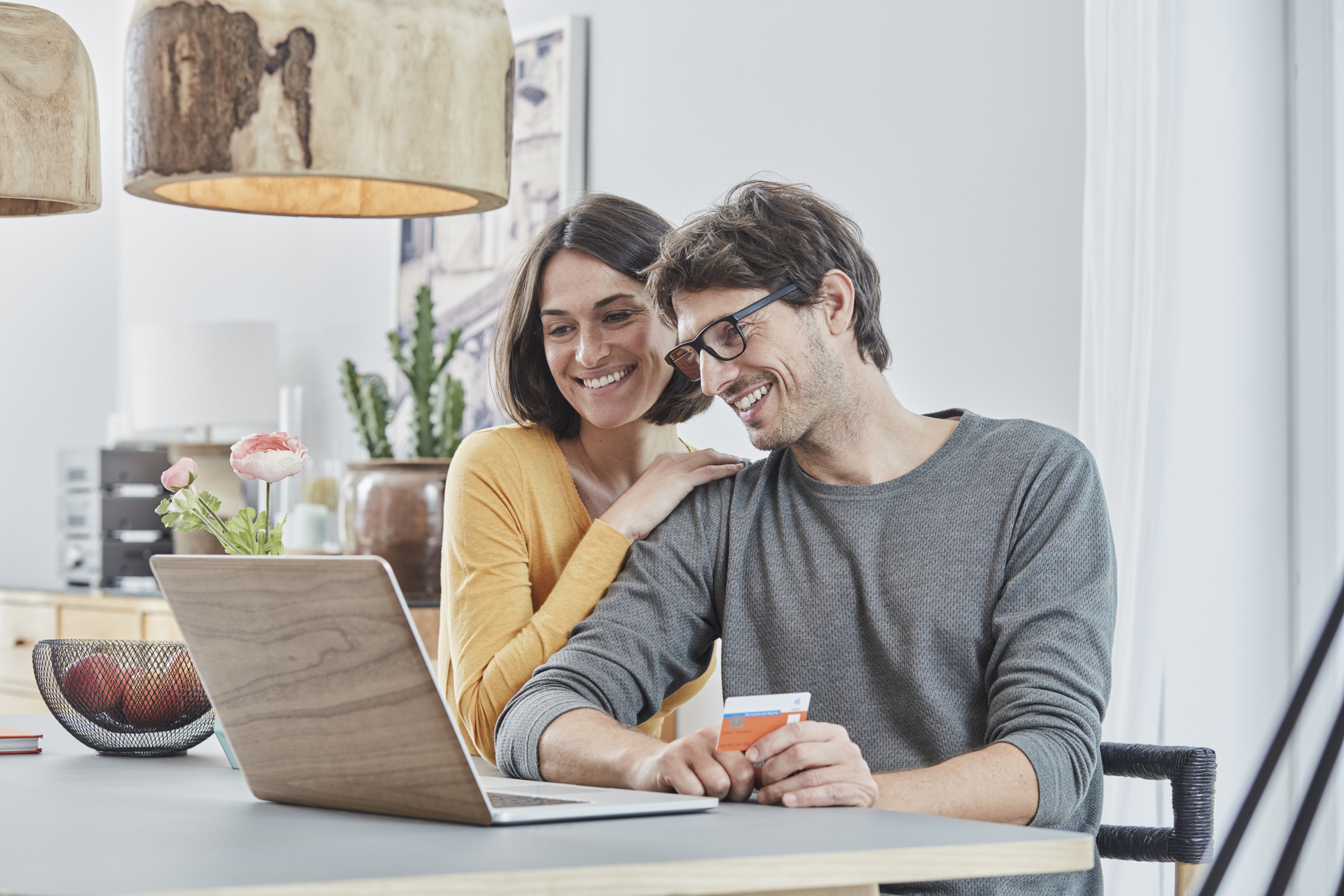 Happy couple with a card using laptop on table at home