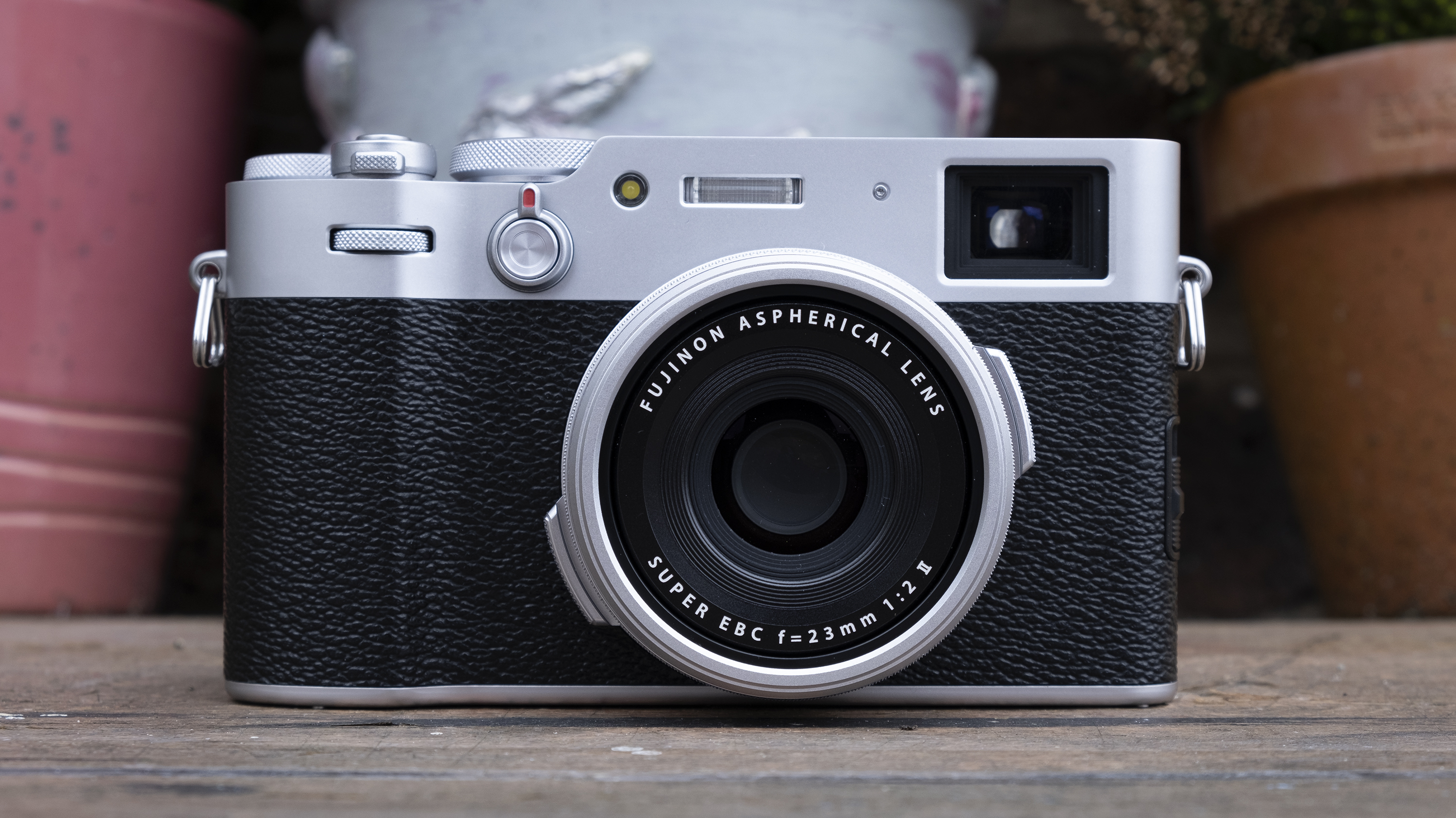 The Fujifilm X100V compact camera in front of flower pots