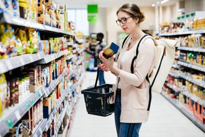 A woman reading the label on a food item while shopping for groceries in a supermarket