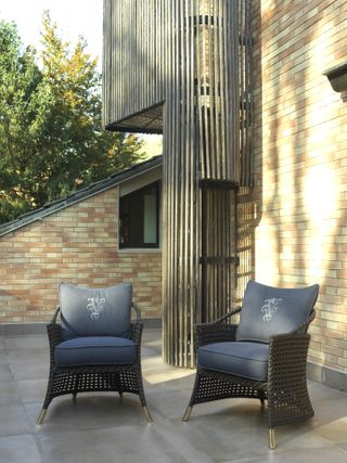 Sunny outside tiled area with two comfortable chairs next to facebrick house