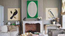 A neutral living room with a large brick fireplace and statement green wall art above. To either side are large bird pictures. There is a neutral beige patterned sofa, opposite a brown and white geometric sofa.