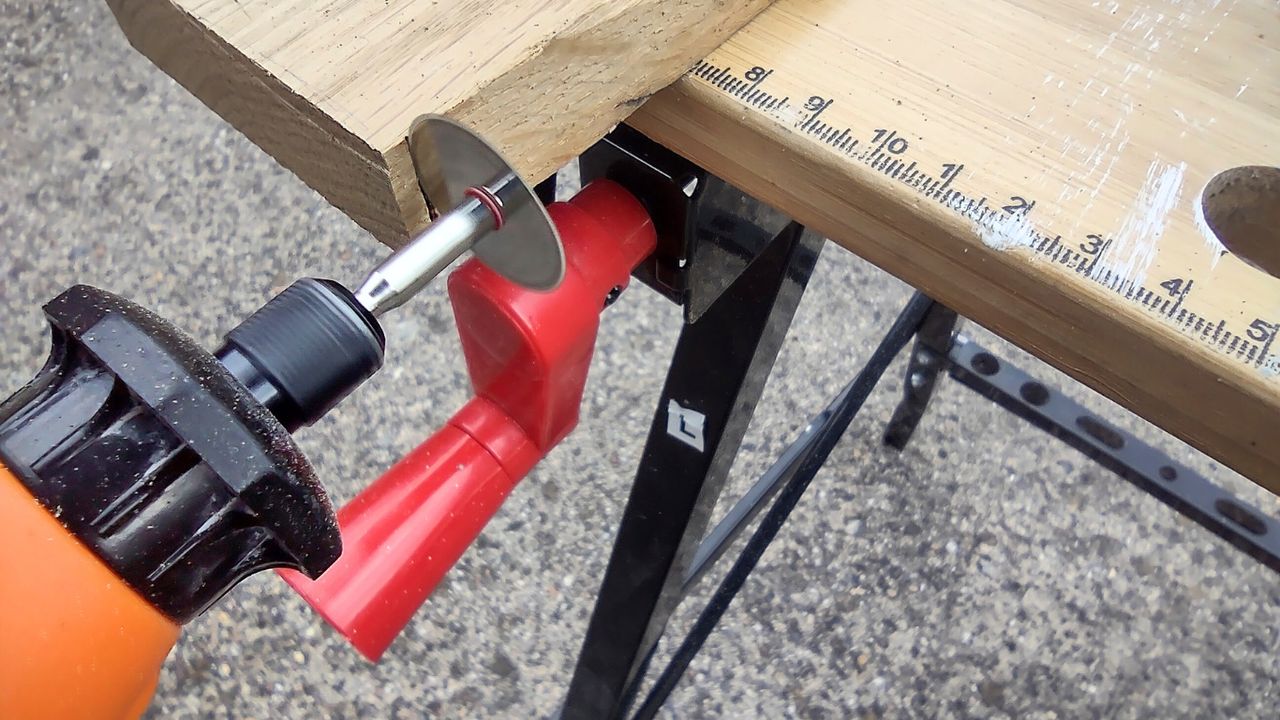 An orange rotary multi tool being used to cut into a wooden board