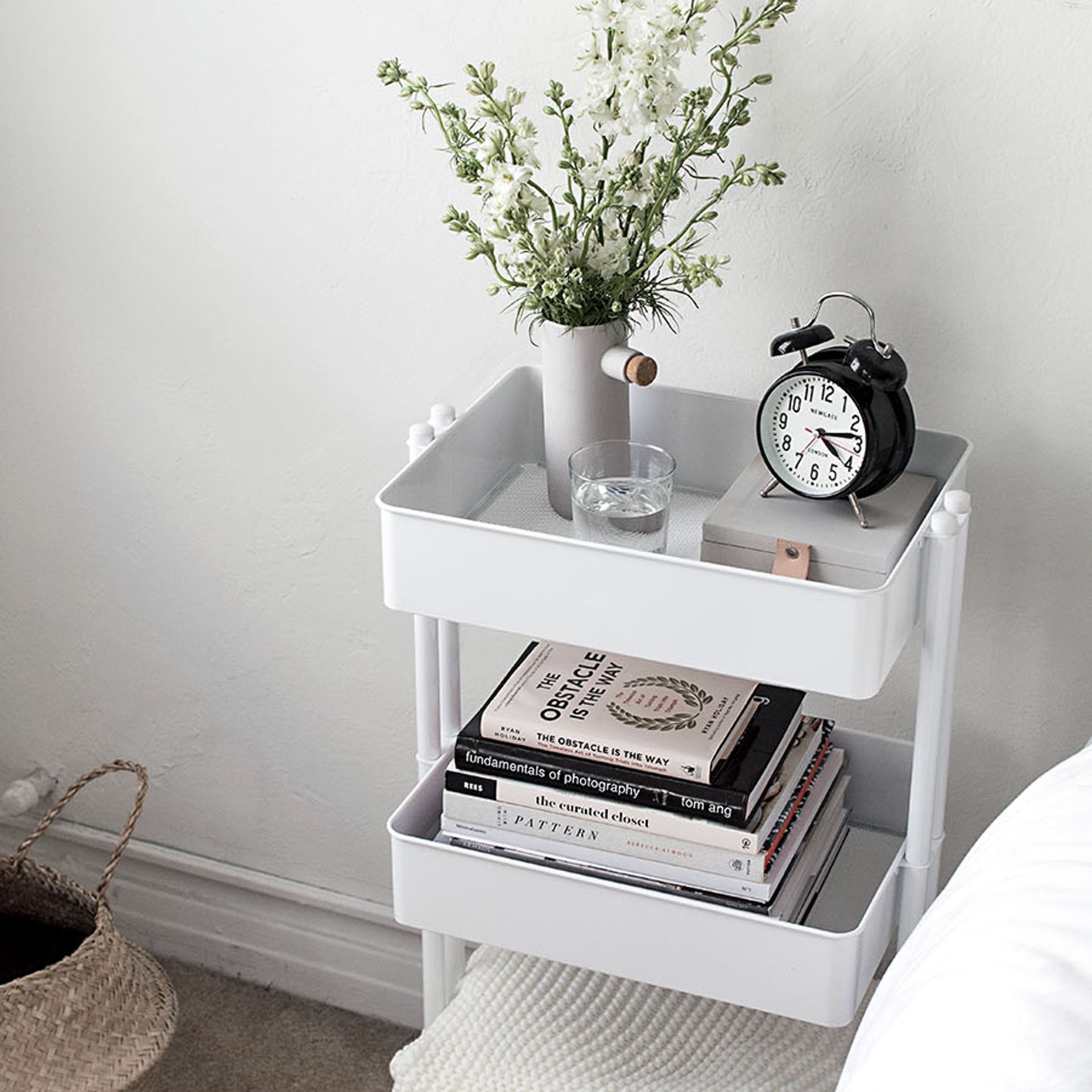 Troli putih digunakan sebagai meja samping tempat tidur yang memajang kebutuhan sehari-hari