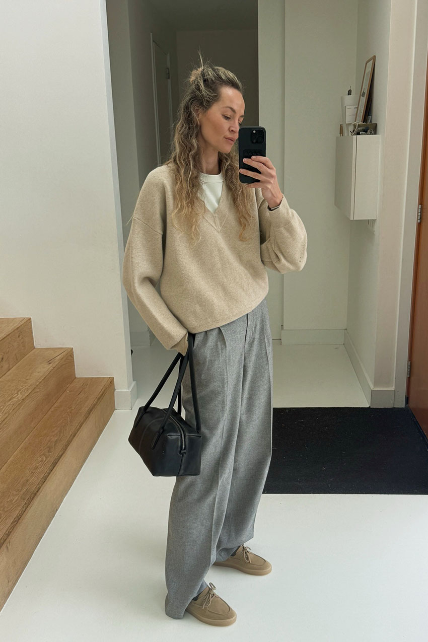 A woman wearing a beige sweater and gray pants.
