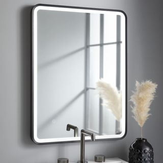 Mirror with black frame on grey wall above wooden unit