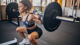 Woman performing a barbell back squat in a squat hold, view is head side on