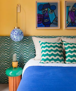 yellow painted bedroom with a wide green geometric headboard, a hanging pendant light and mid century abstract wall art in a bright blue