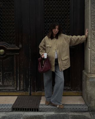 @francescasaffari wears a beige canvas jacket, grey jeans, brown trainers and a burgundy woven handbag