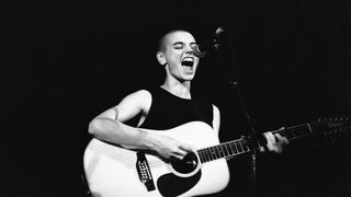 Sinead O'Connor performing on stage with a guitar in 1988