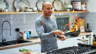 Man stir-frying vegetables in a wok in a home kitchen