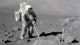 An astronaut in a white spacesuit stands on the surface of the moon with a metal detector.