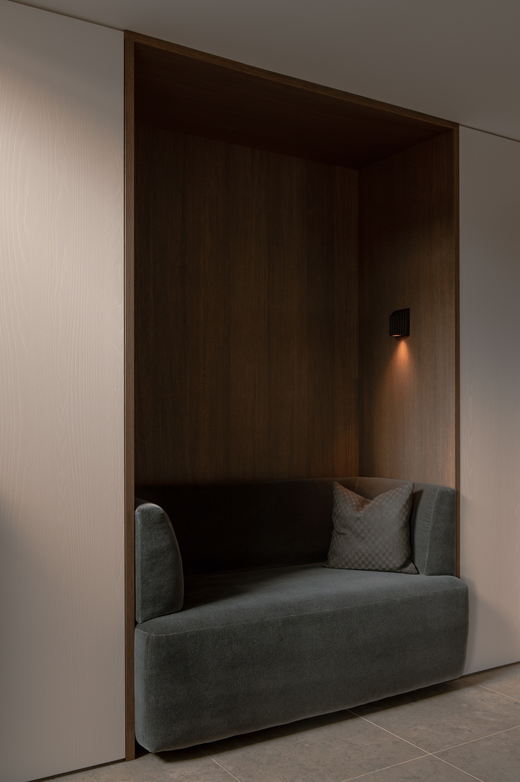 a wood-panelled alcove with a grey sofa inside and a soft, warm wall light inside the alcove