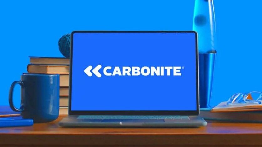 A laptop with the Carbonite logo on screen sitting on a desk in front of a blue wall