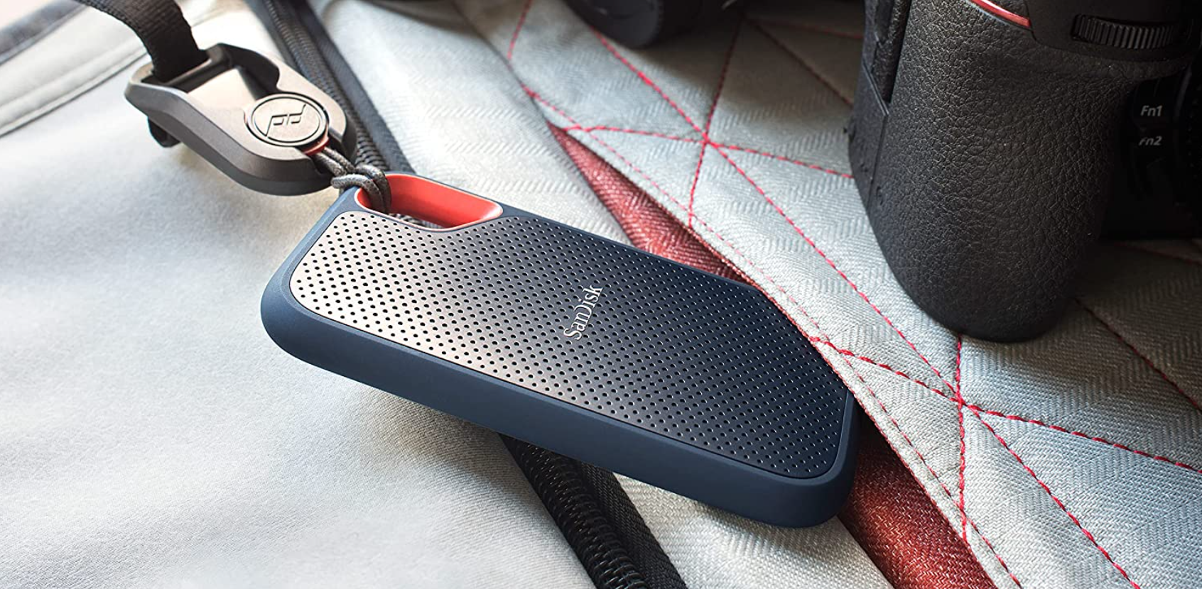 SanDisk Extreme Portable SSD in black on a carabiner loop next to a camera.