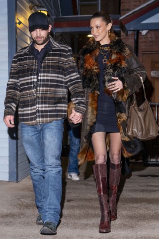 Bella Hadid steps out of Matsuhisa in Aspen with her boyfriend, Adan Banuelos, following a cozy dinner, looking radiant in a dark brown fur-lined coat with multicolored detailing. She paired it with a sleek black mini dress, semi-sheer tights, and knee-high burgundy leather boots. The couple, dating for over a year, looked happy and relaxed as they made their way through the snowy evening.