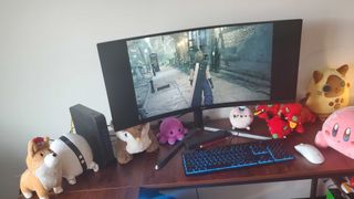 a large curved monitor on a wooden desk with several plushies under it