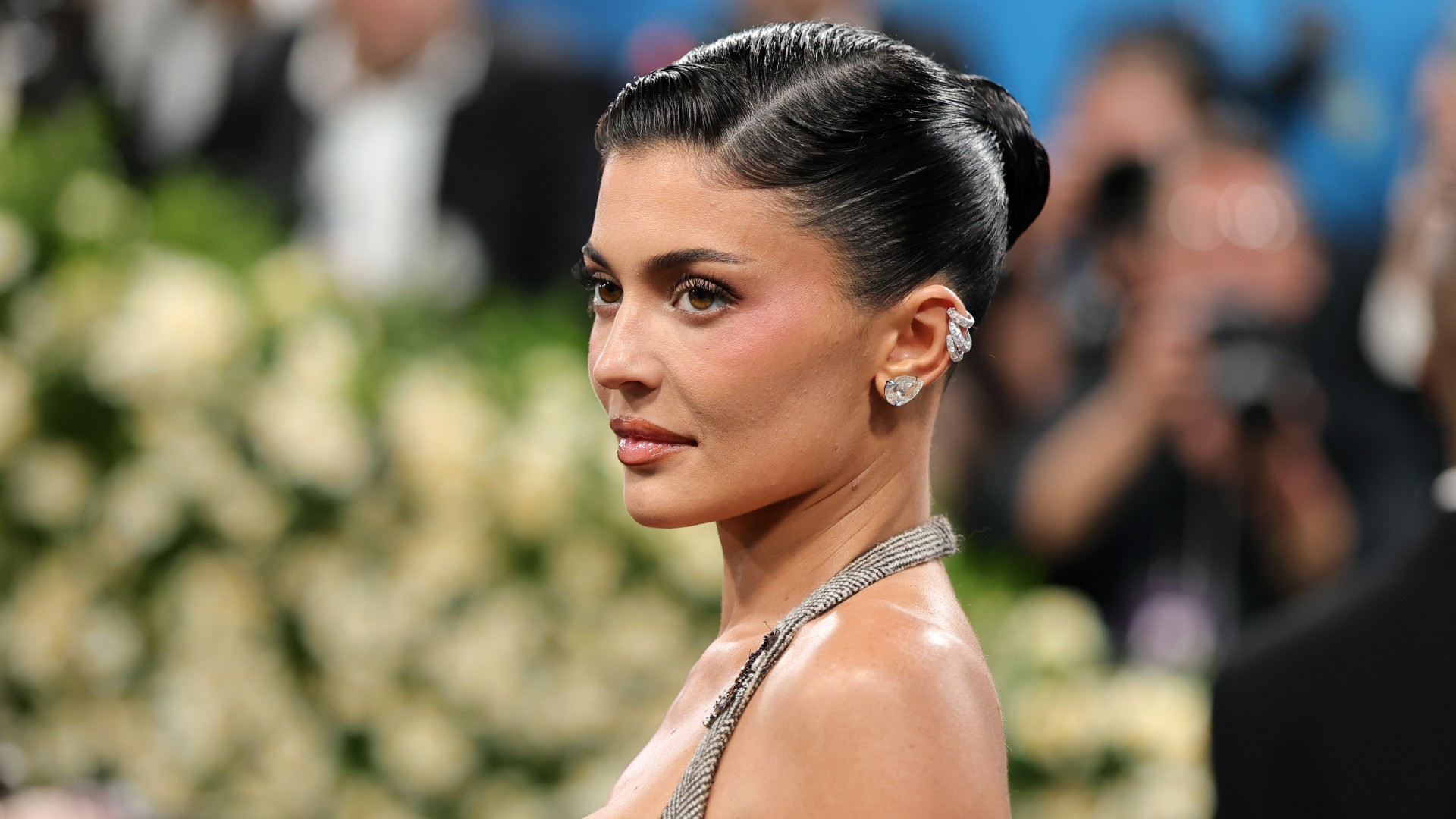 a woman photographed in front of a crowd wearing a tight bun and silver earrings