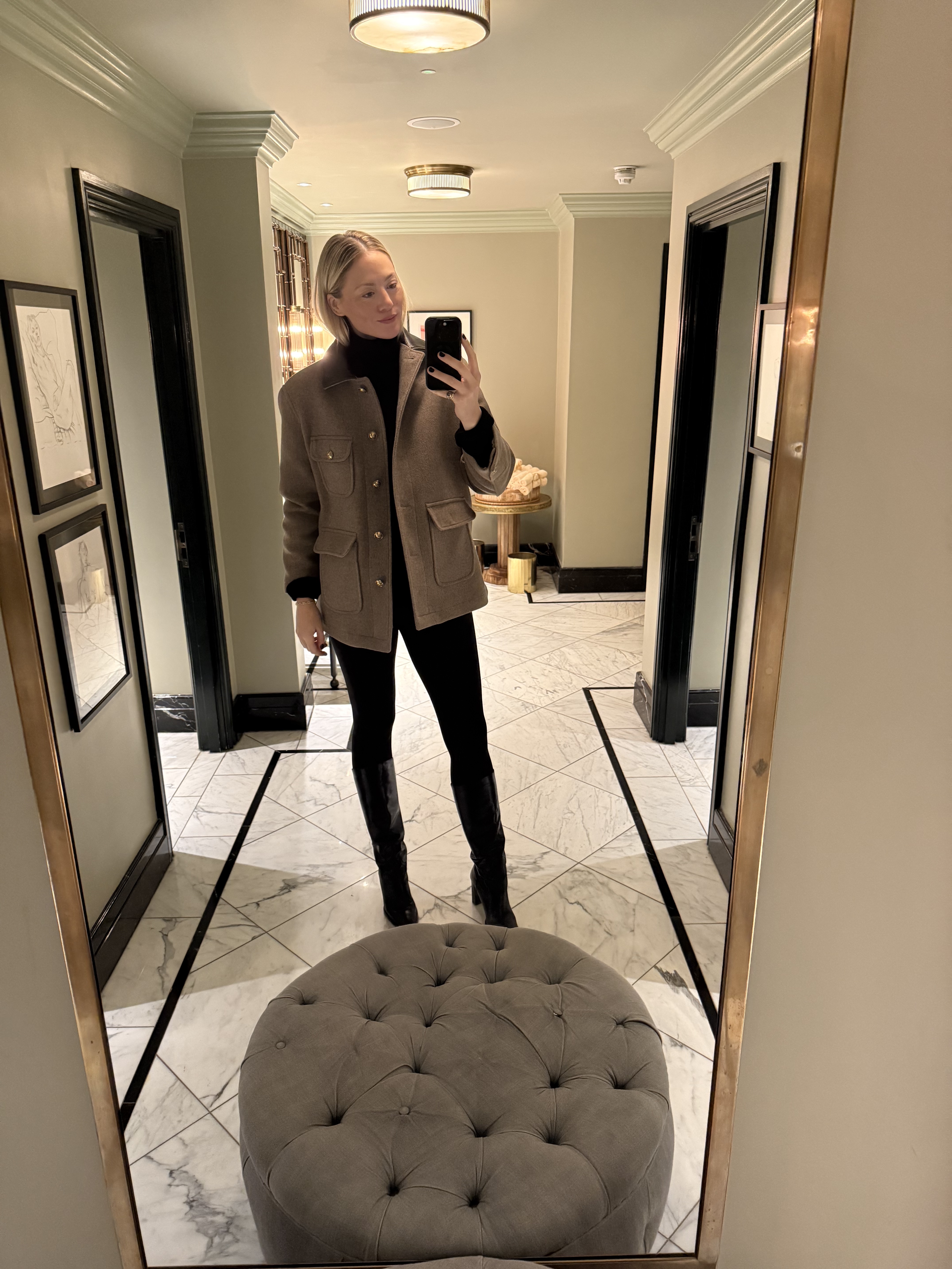 Brooke Ely Danielson standing in front of a mirror wearing a turtleneck, jeans, and a coat