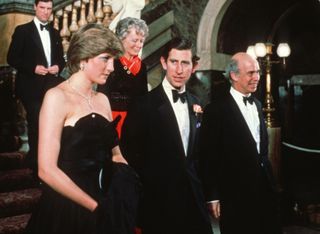 Princess Diana wearing a black strapless gown standing next to Prince Charles wearing a tuxedo on a staircase in 1981