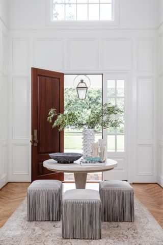 White entryway with high ceilings and a table with three fringe stools around it.