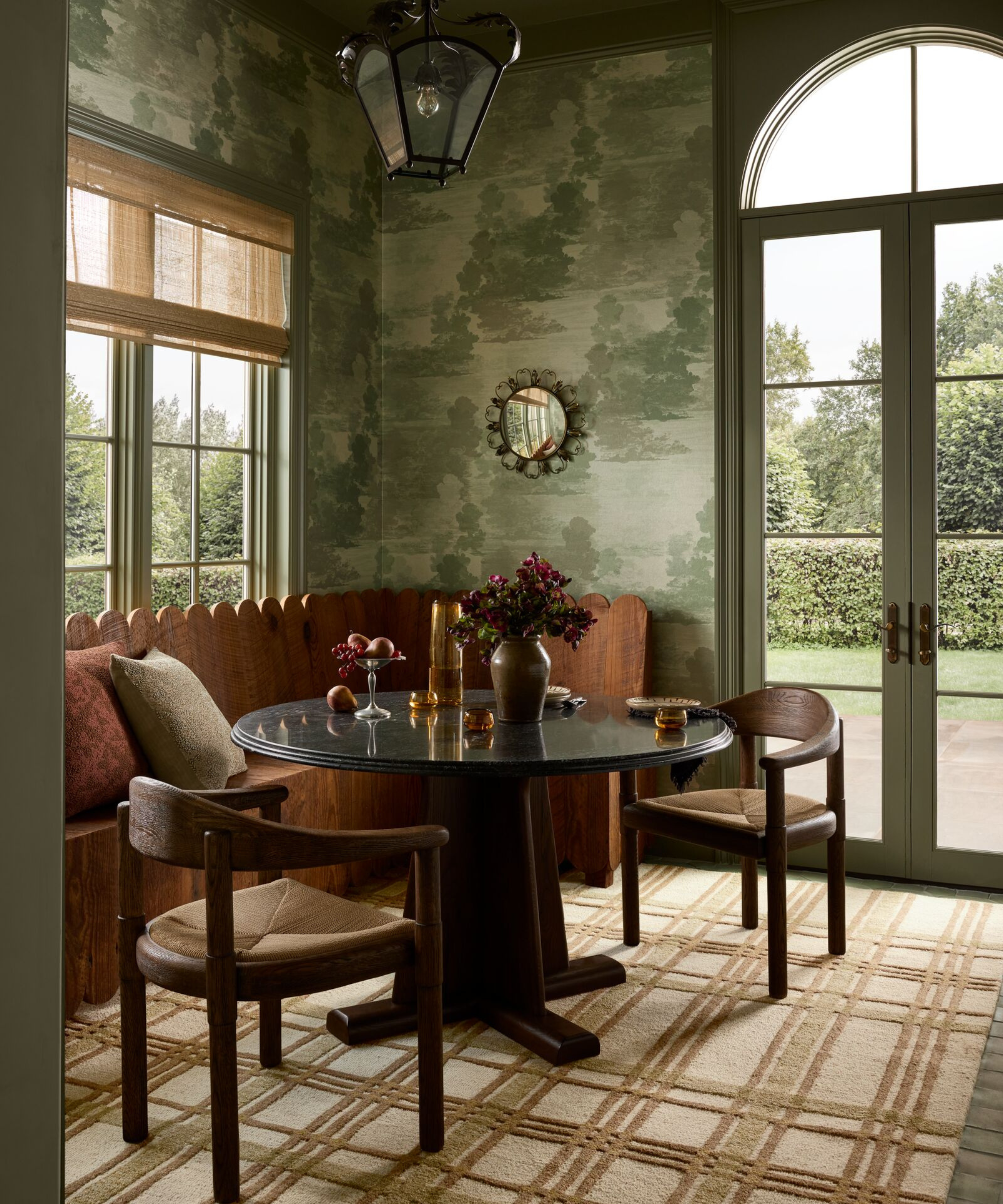 a dining nook with green wallpaper, a striped brown rug, a circular table, two chairs, and a built-in bench