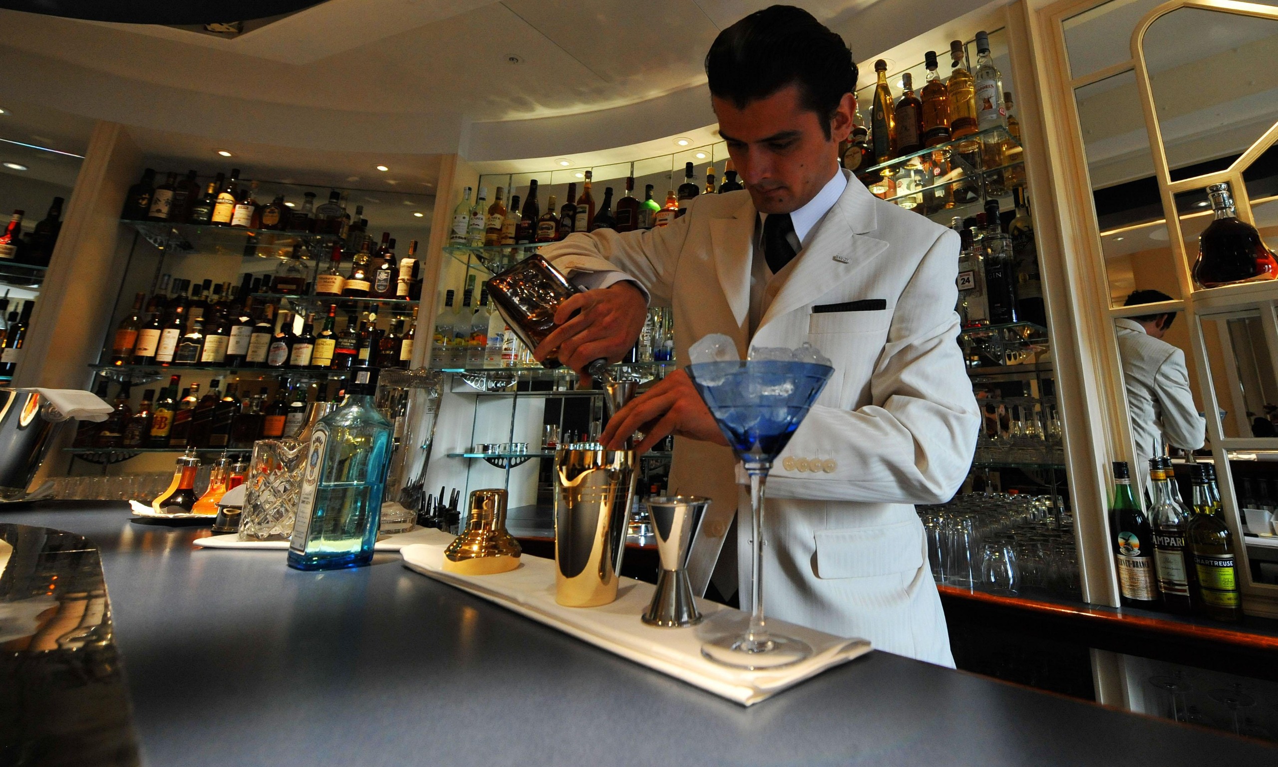 A man in a white suit makes a cocktail on the counter of the American Bar at the Savoy
