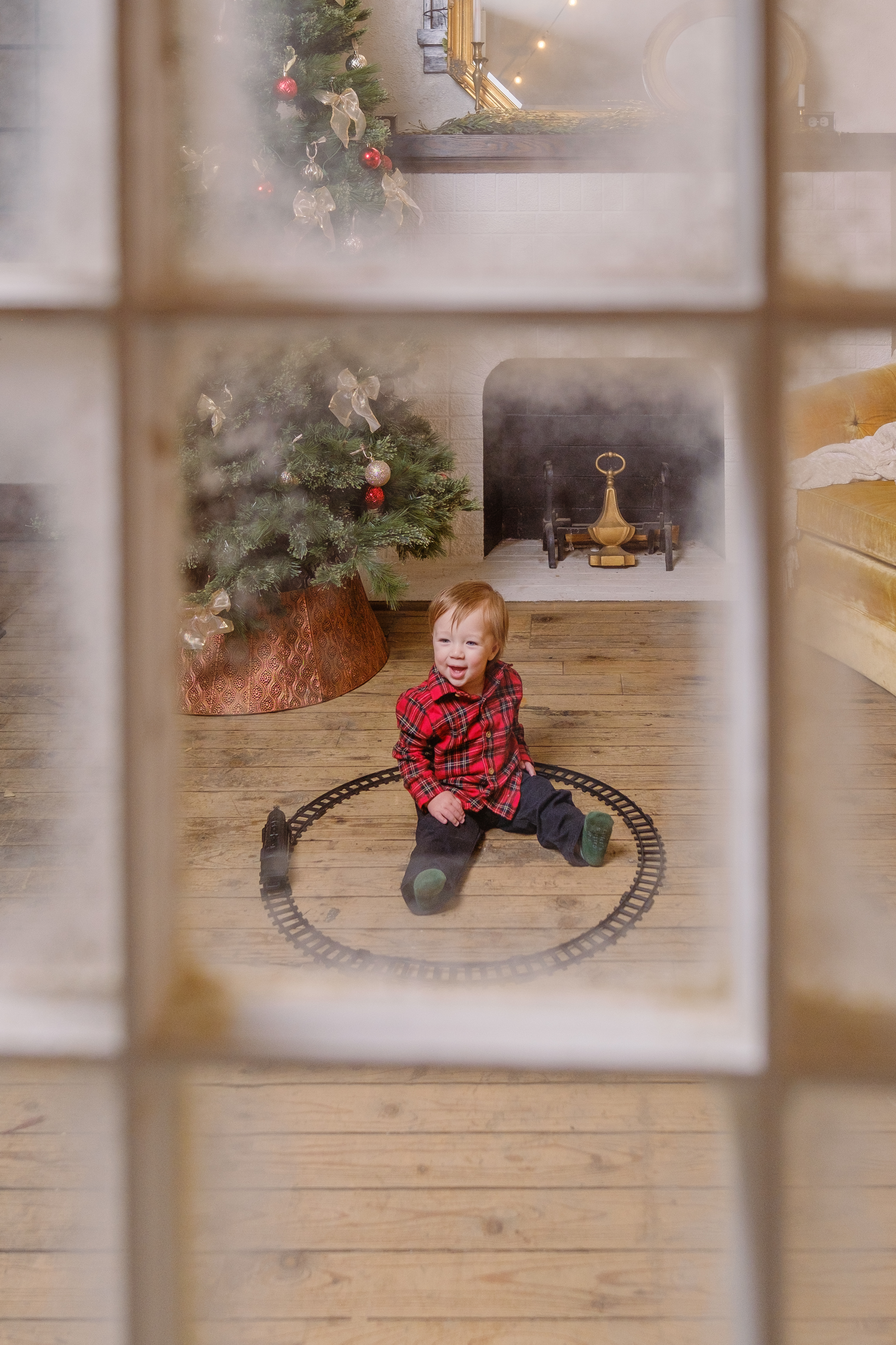 A child with a toy train framed by a snowy Christmas window