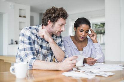 Worried couple reading bills at table in home