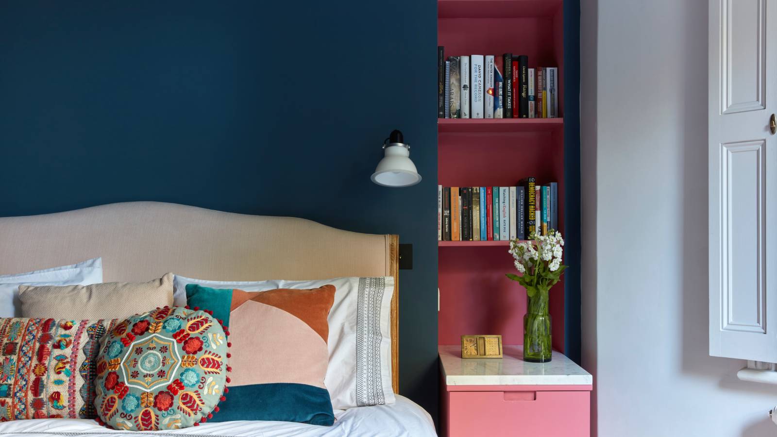bedroom with alcove next to bed painted pink in contrast to blue bedroom walls and white window shutters