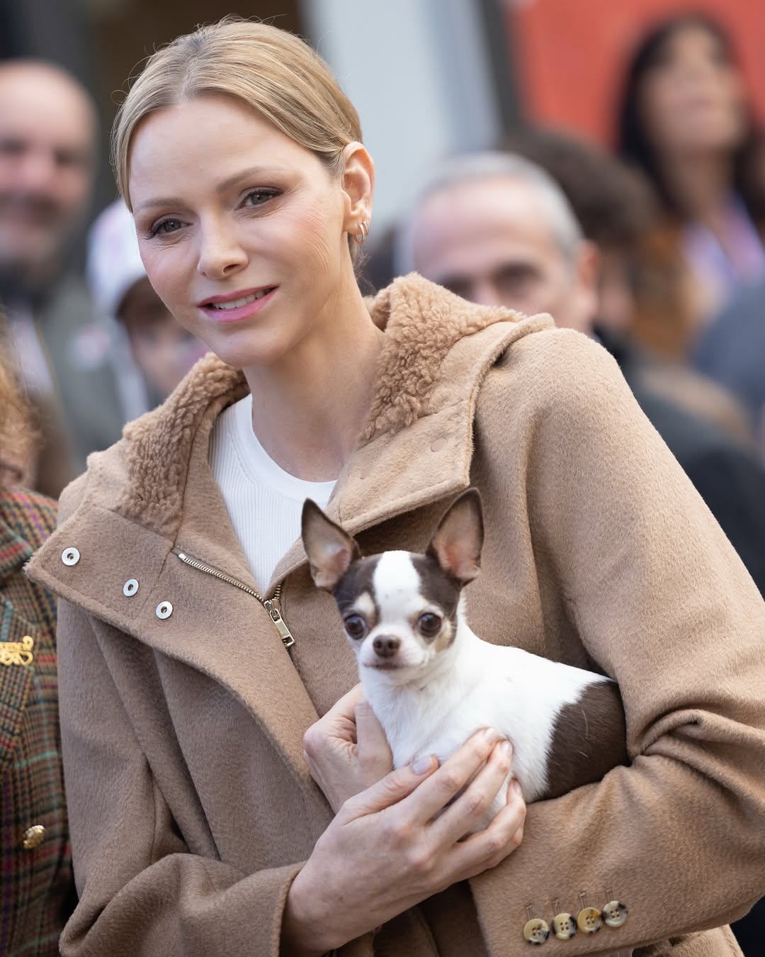Princess Charlene holding a dog wearing a tan coat