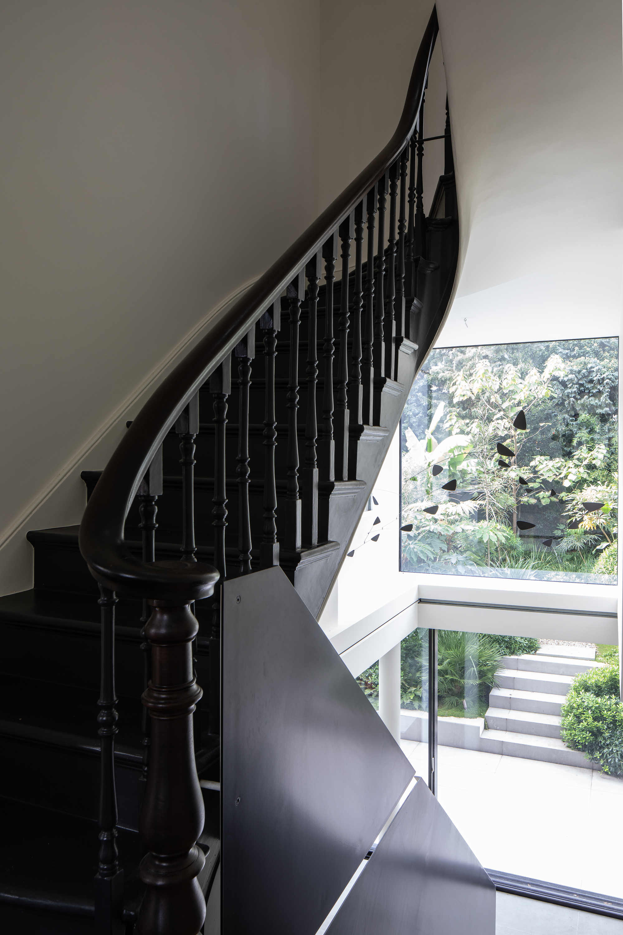 A curved black staircase with a traditional balustrade and a view out of a window