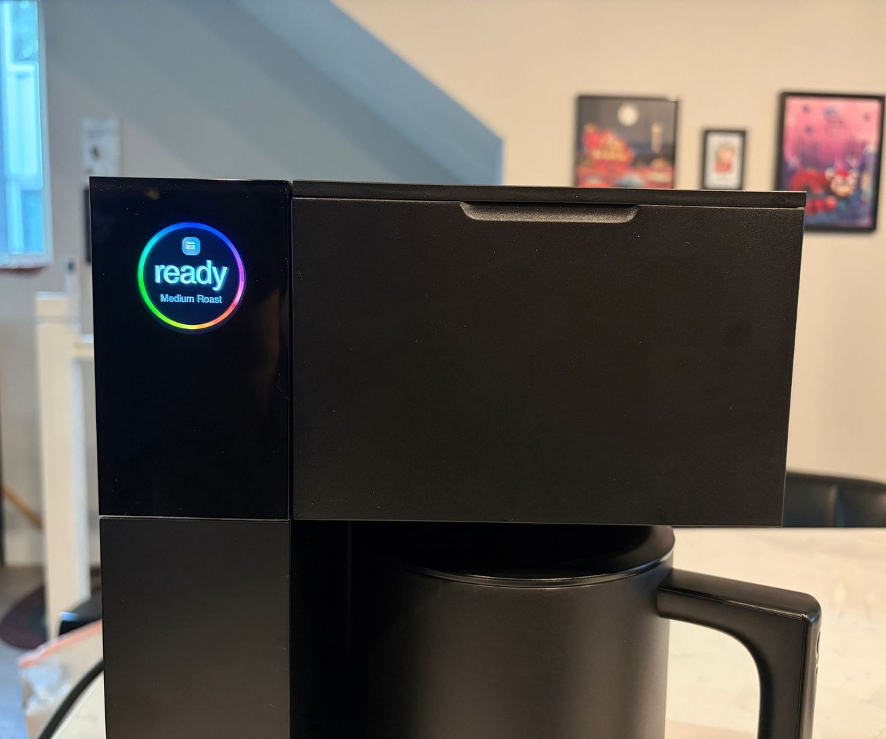 The top of a blocky black coffee maker with an LED screen in the top left corner, with 'ready' on it.
