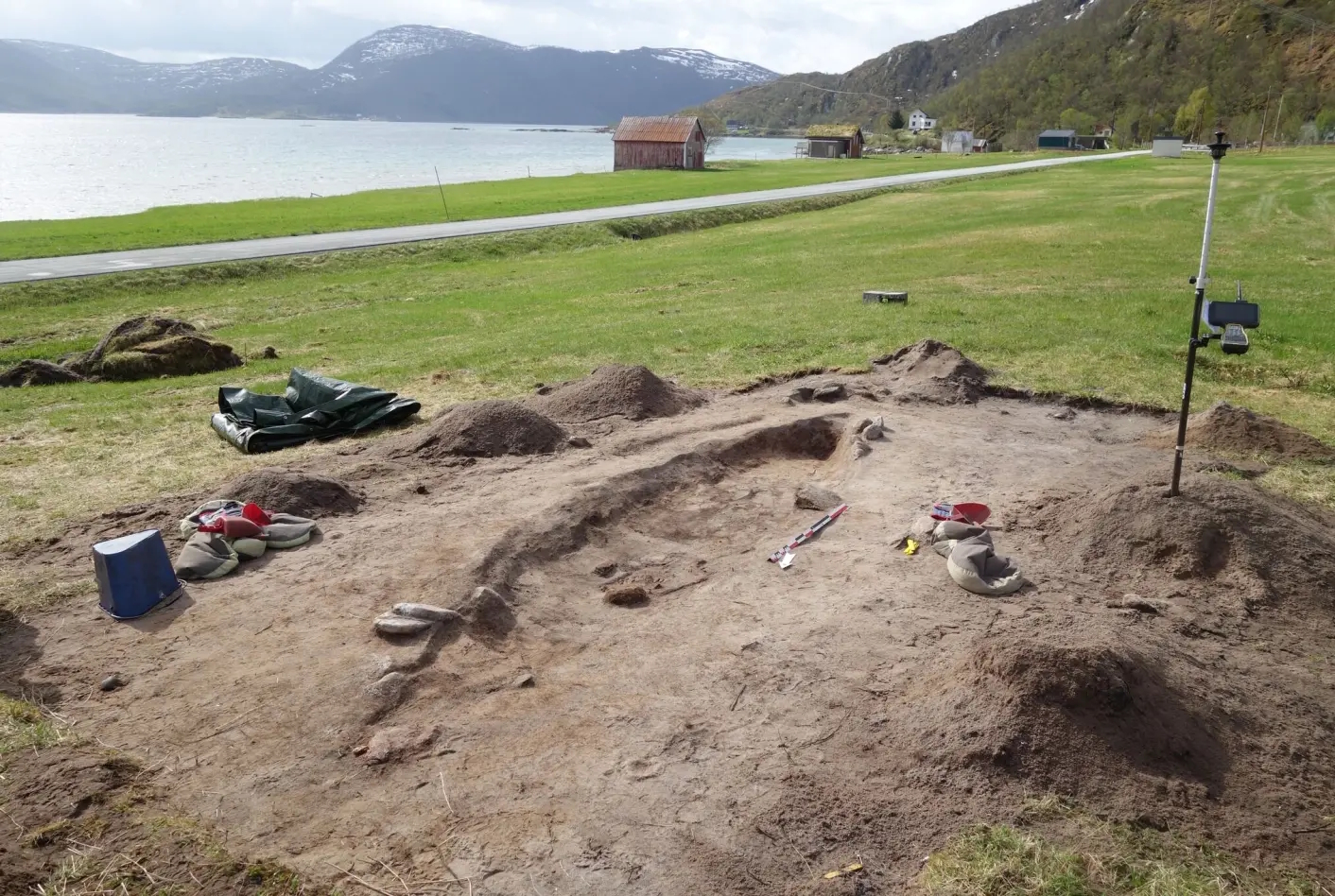 a view of a grave excavation site by a body of water with mountains in the distance