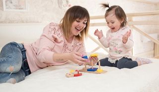 A mom and her baby girl play together with a toy.