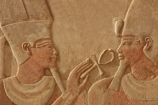 A bas relief of the god Amun-Ra making the gift of life (ankh) to the pharaoh Thutmoses IV. Sculpted in red quartzite, with traces of original paint remaining.