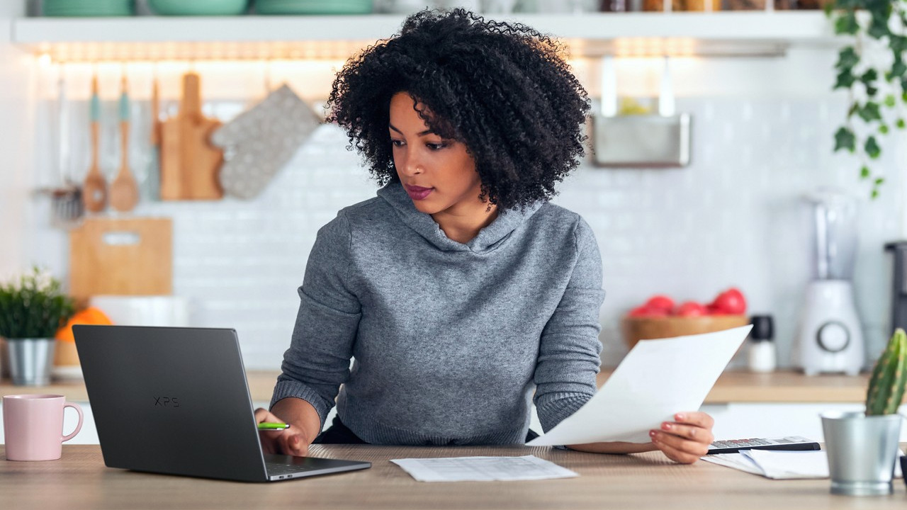 Dell XPS 14 being used by a person sat at a desk holding a piece of paper