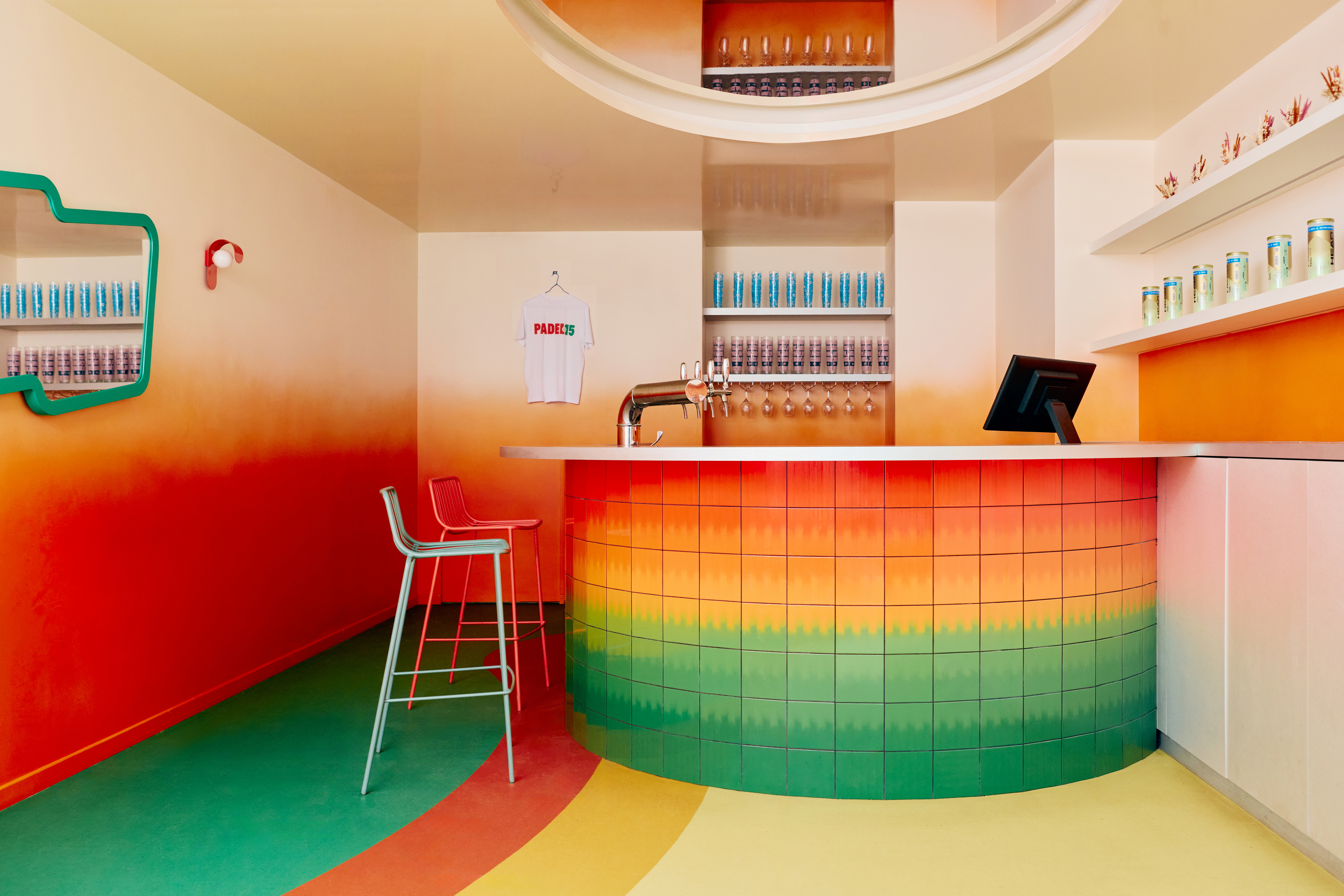 The restaurant and bar of a sports club features gradient green, orange, ochre, and yellow floors, walls, bar tiles, and furniture, each characterized by a whimsical essence.