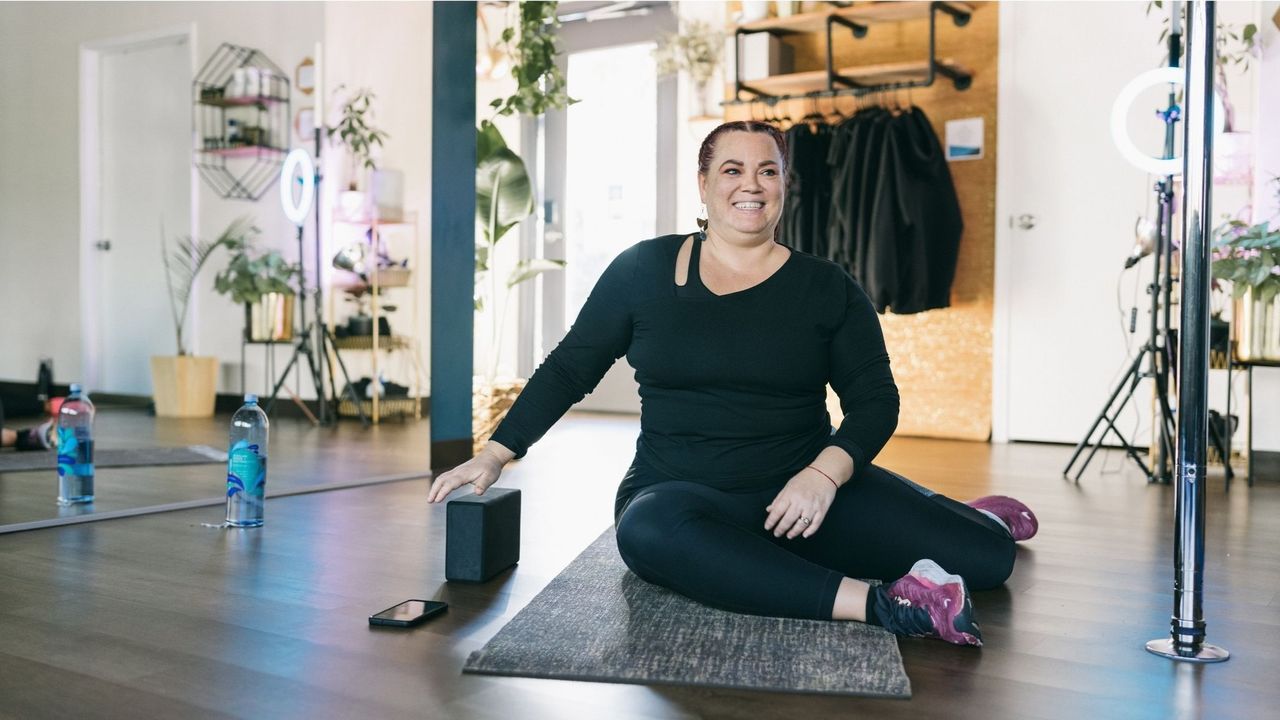 A woman performs a 90/90 hip stretch on a yoga mat in a gym