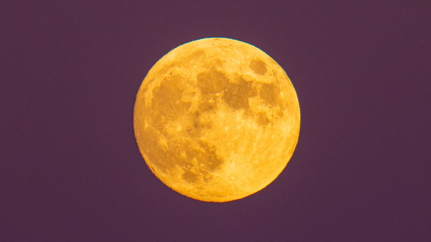 A photograph of the full moon, looking yellow against a purple sky