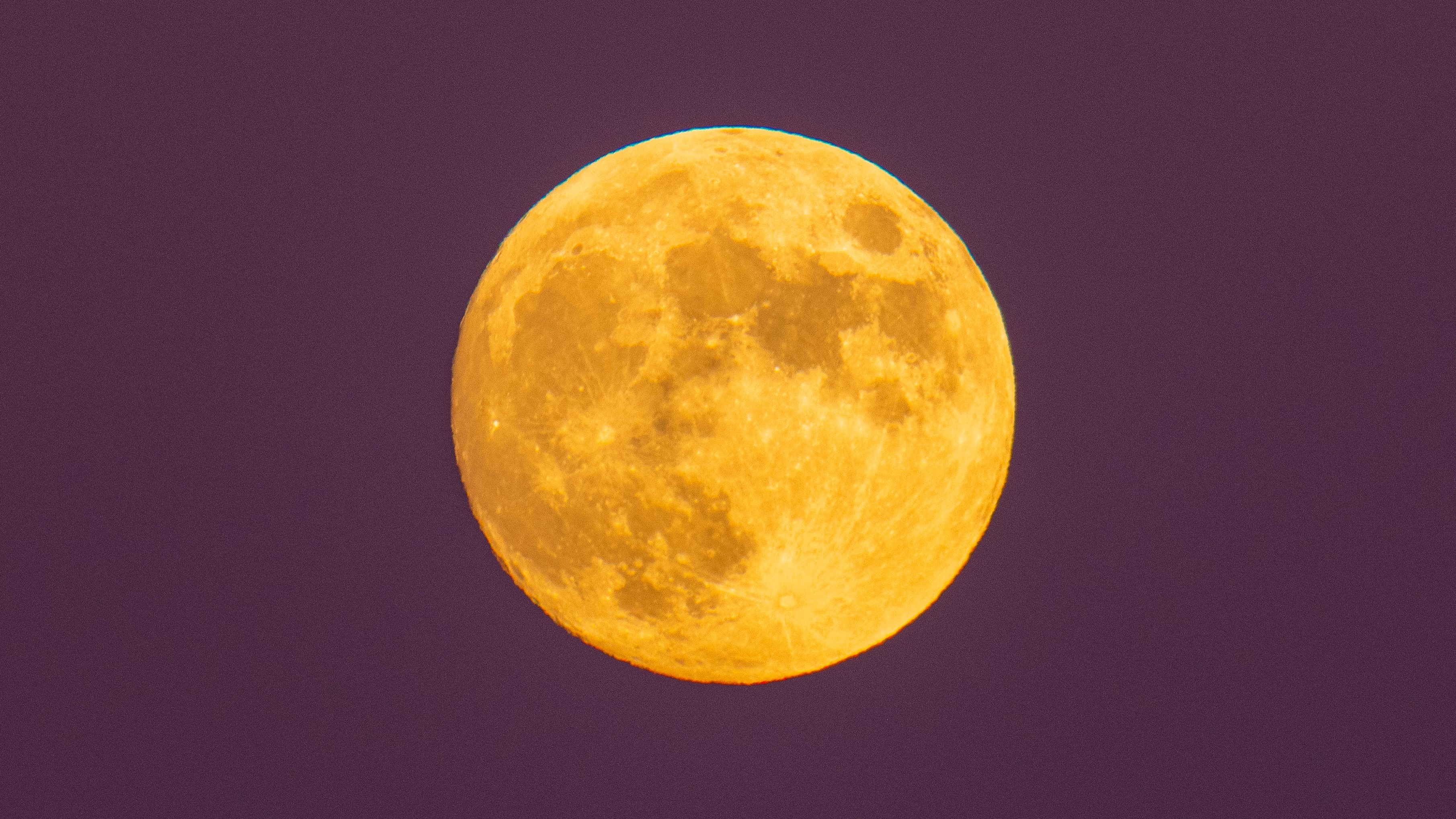 A photograph of the full moon, looking yellow against a purple sky