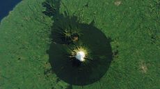 A satellite image of a volcano with a near=perfect ring of dark green trees around its peak