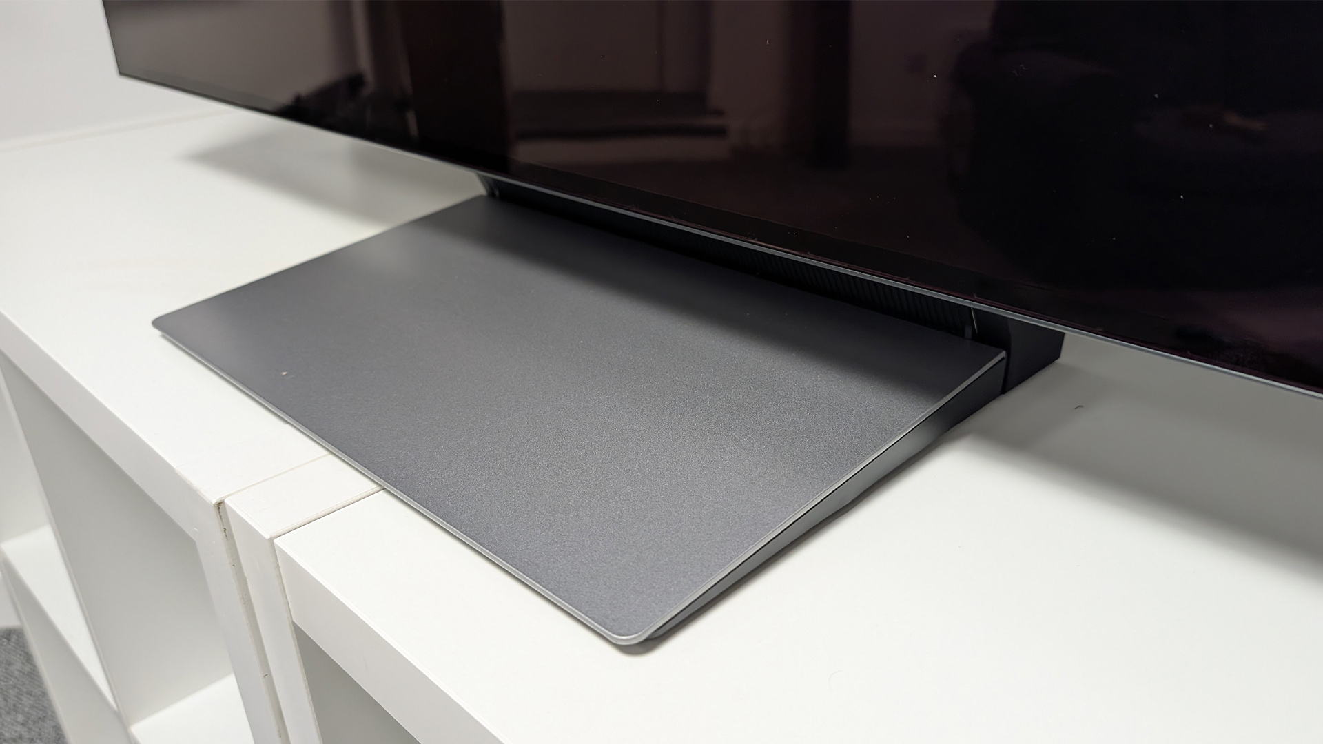 Samsung S90F 48-inch OLED TV on white wooden furniture detail of bottom of TV and stand
